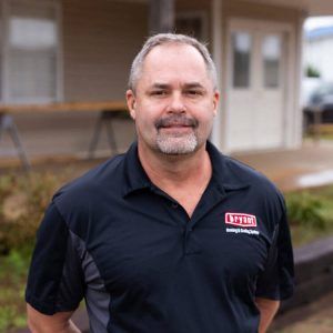 A man in a black shirt is standing in front of a house.