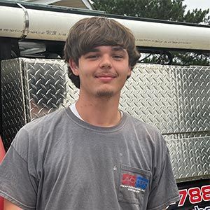 A young man in a gray shirt is standing in front of a truck.