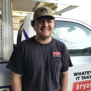 A man wearing a hat is standing in front of a truck that says what 's it take bryan