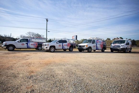 A row of trucks and vans are parked in a gravel lot.