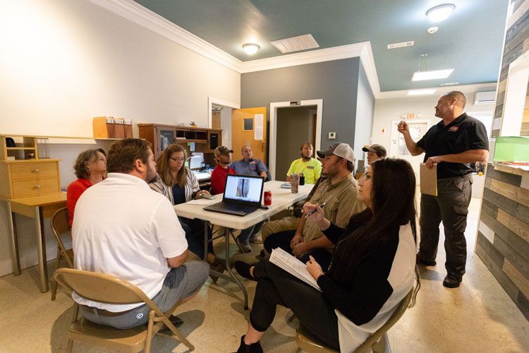 A group of people are sitting around a table with laptops in a room.