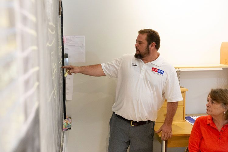 A man is pointing at a blackboard while a woman sits at a desk.