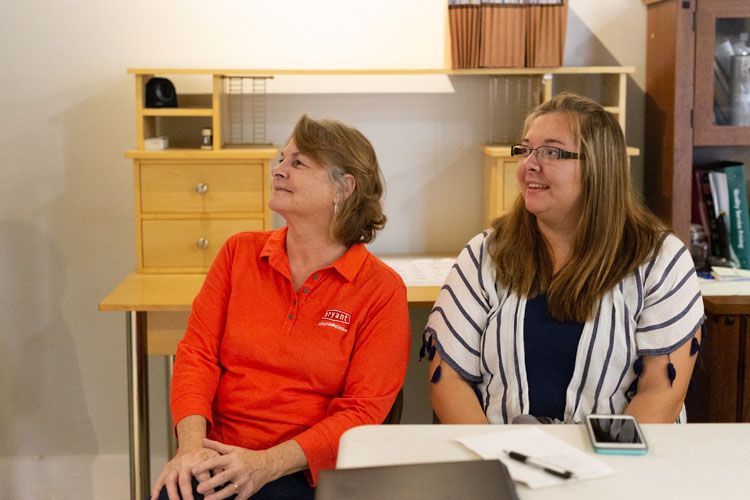 Two women are sitting at a table with a laptop.