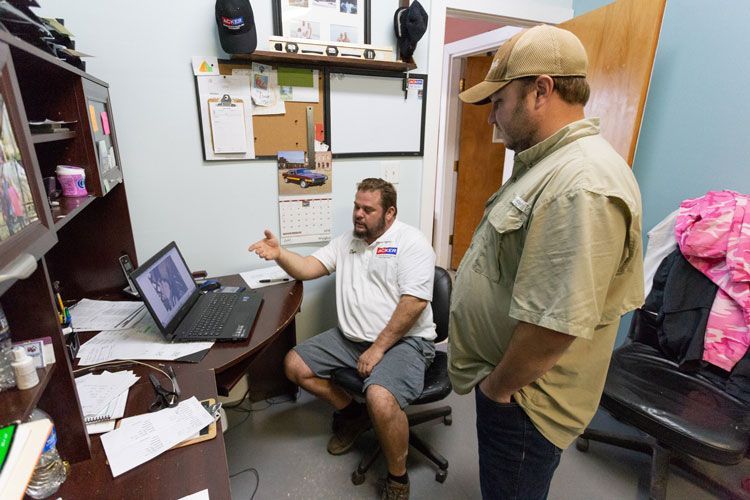 Two men are standing in a room looking at a laptop.