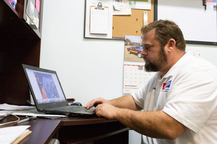 A man in a white shirt is typing on a laptop