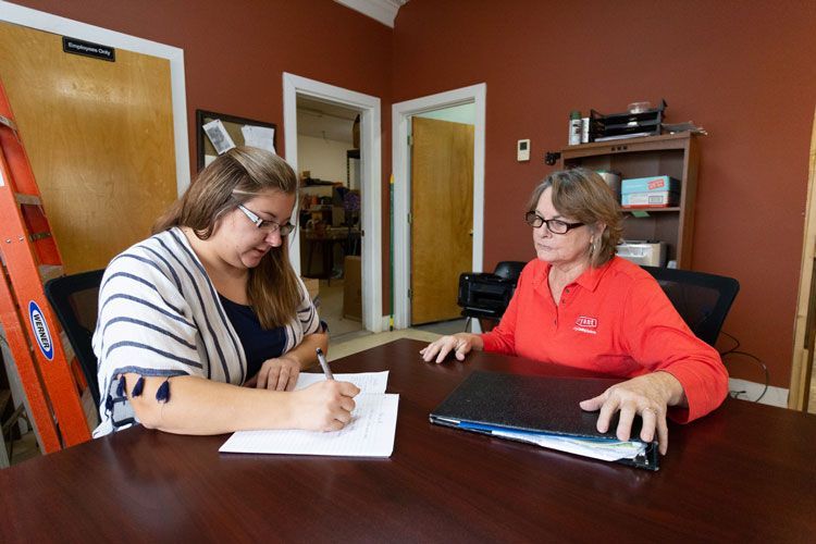 Two women are sitting at a table writing on a piece of paper.