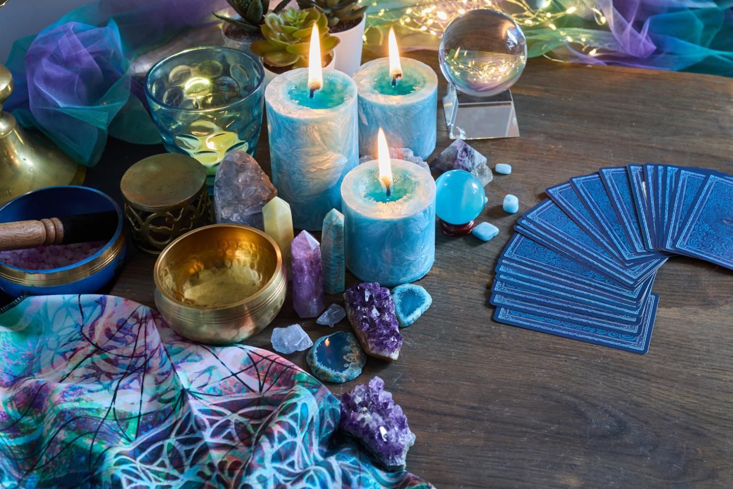 Mystical scene: lit candles, tarot cards, crystals, and singing bowls on a wood table, with blue and purple hues.