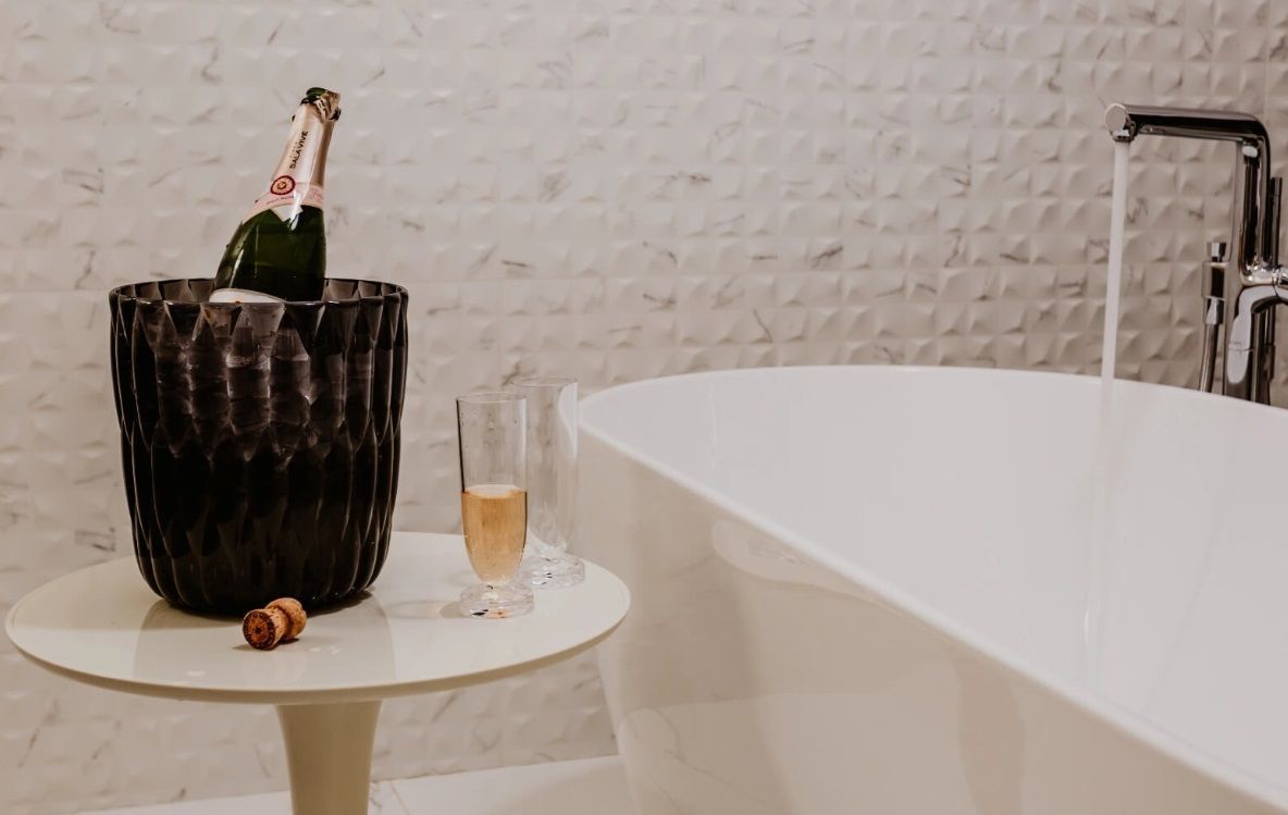 Un cubo de champán y una copa de champán están sobre una mesa al lado de una bañera.