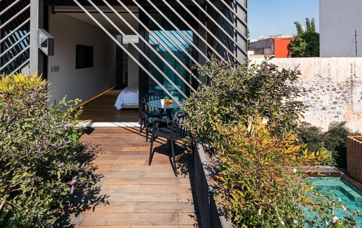 Una pasarela de madera que conduce a una sala con una mesa y sillas junto a una piscina.