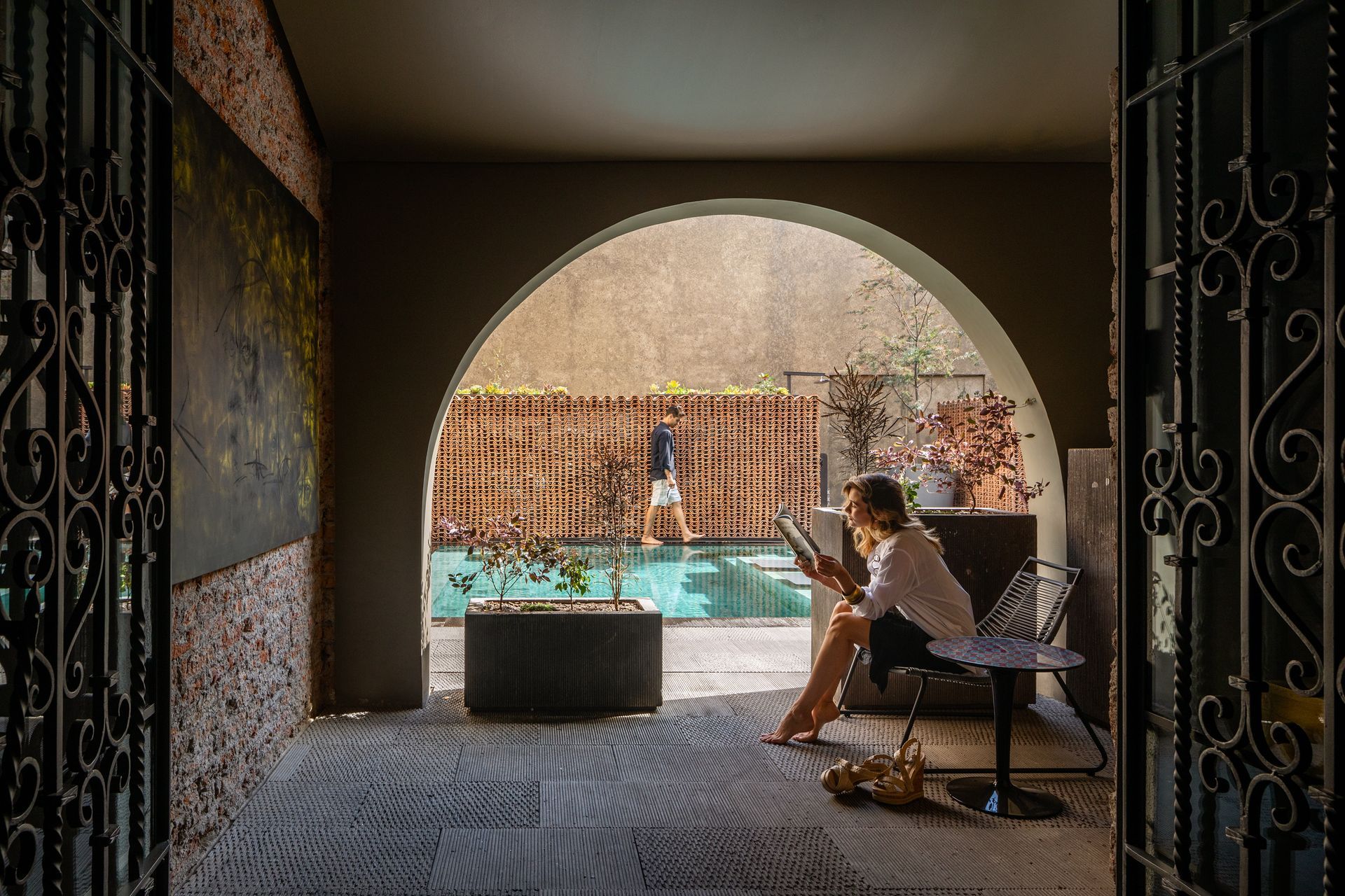 Una mujer está sentada en una silla leyendo un libro frente a una piscina.