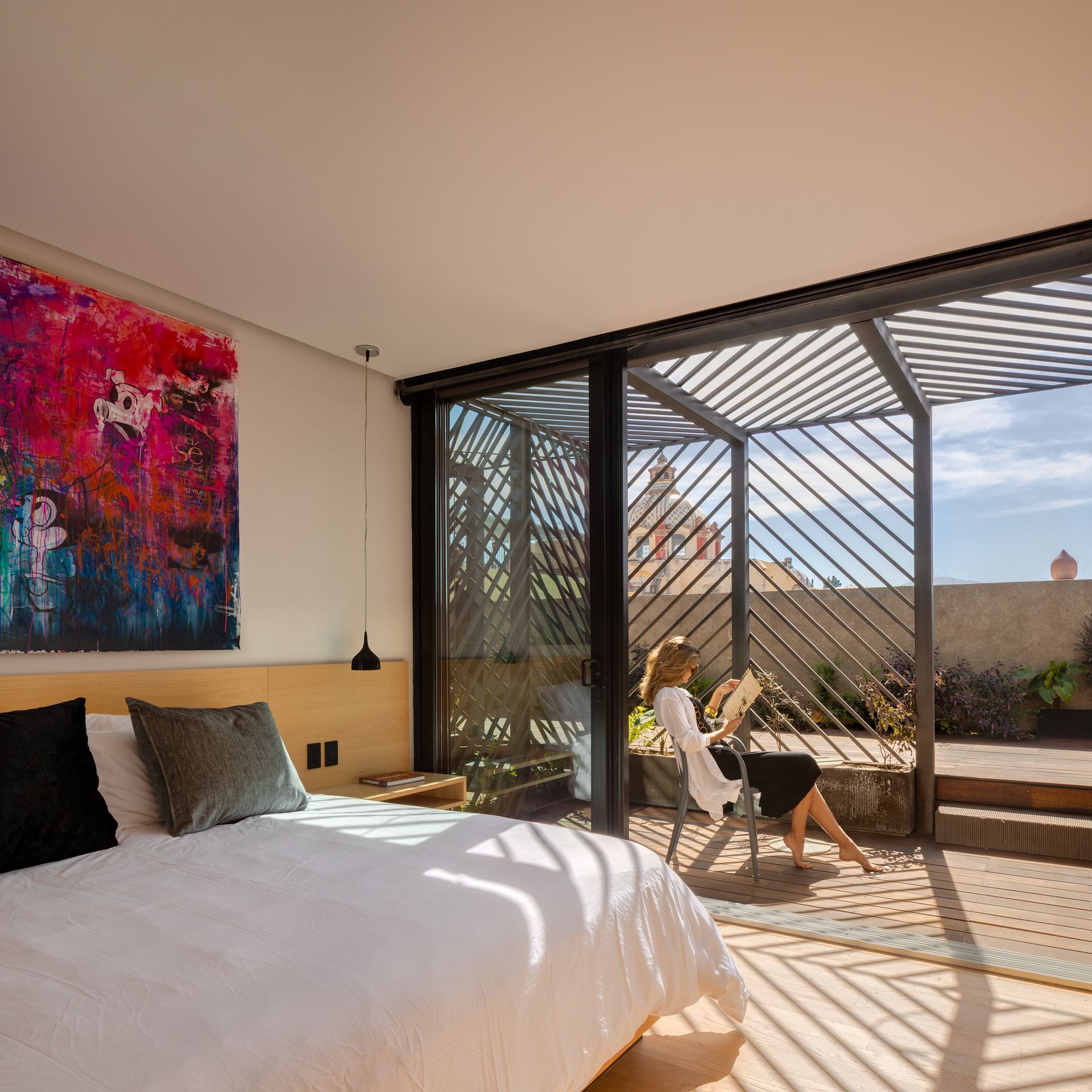 Una mujer está sentada en una silla en un dormitorio con una ventana grande.