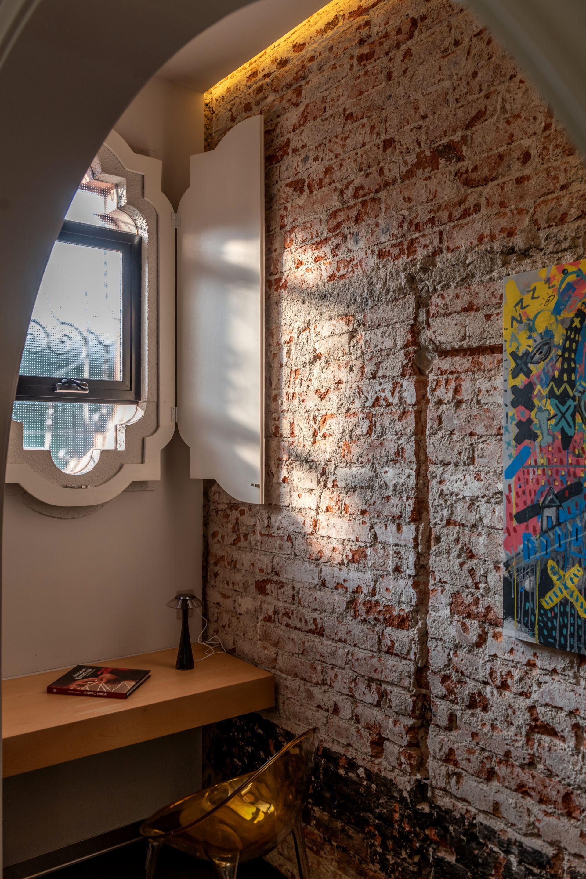 Una habitación con una pared de ladrillos, un escritorio, un espejo y un cuadro en la pared.