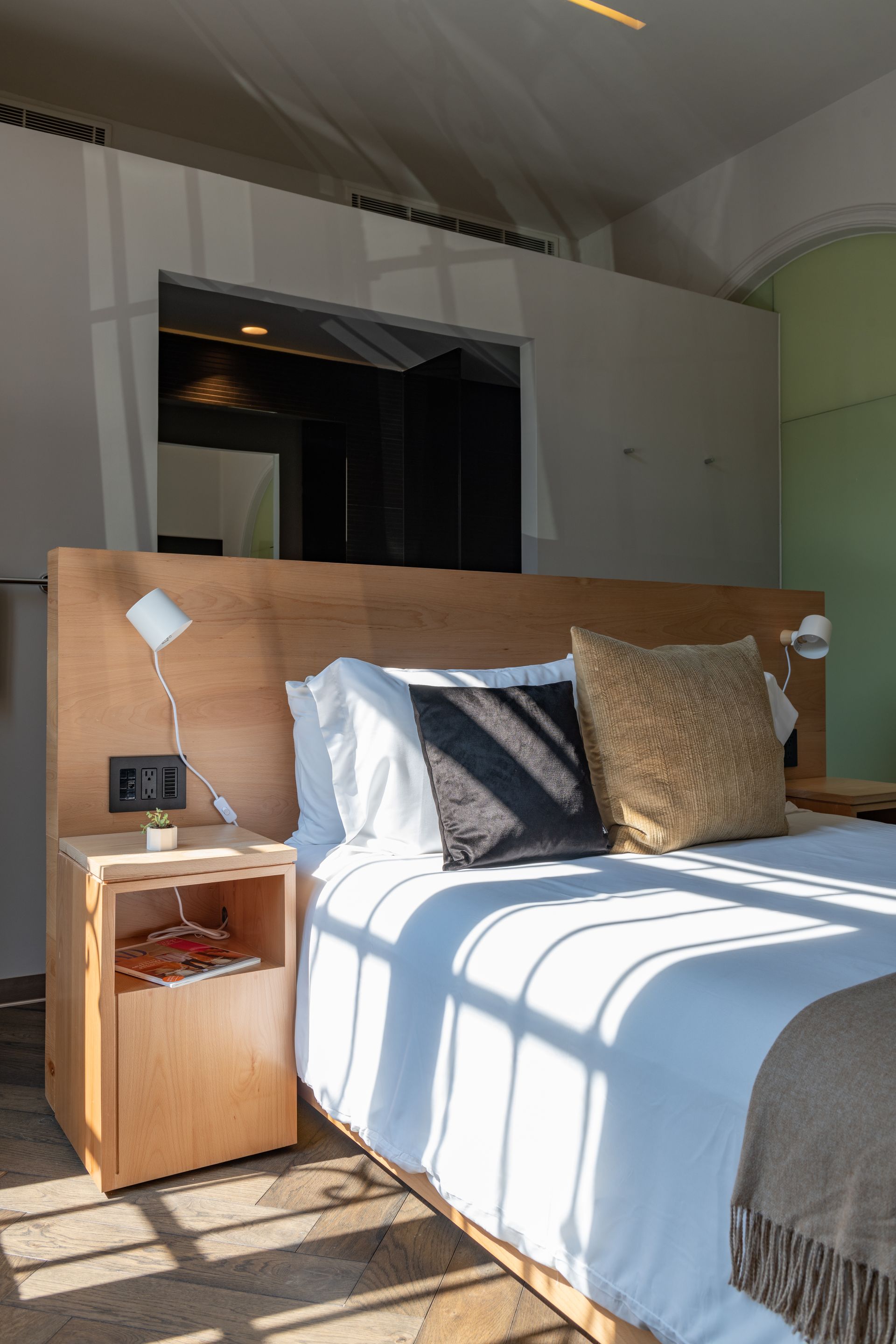 Un dormitorio con cama, mesita de noche, lámpara y espejo.