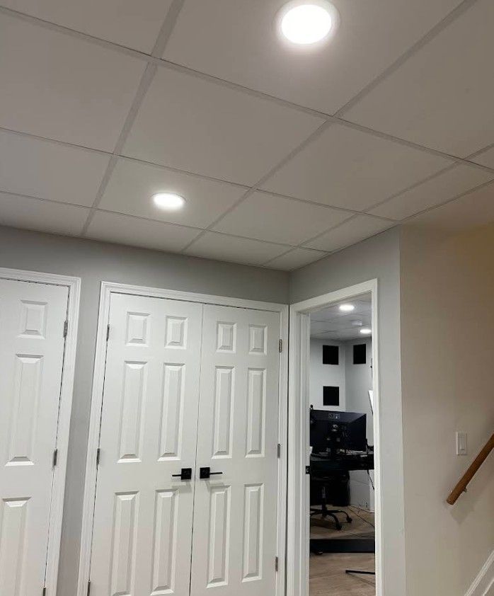 A white drop ceiling with two recessed lights above white double doors and a doorway looking into a home office.