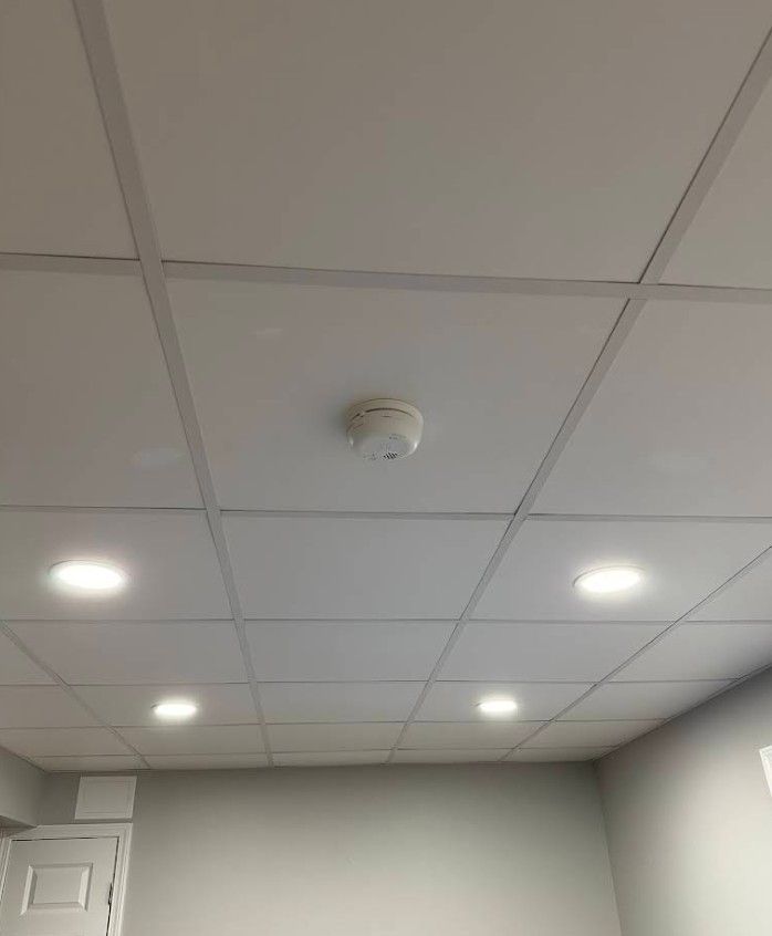 A drop ceiling in an interior space featuring four recessed lights and a central smoke detector.