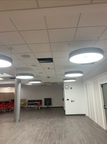 A large, empty room with grey wood-look floors, white walls, and several circular pendant lights hanging from the ceiling.