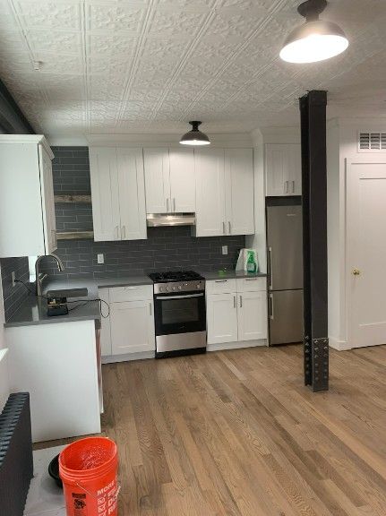 Modern kitchen with white cabinets, dark gray tiled backsplash, stainless steel appliances, and wood floors.