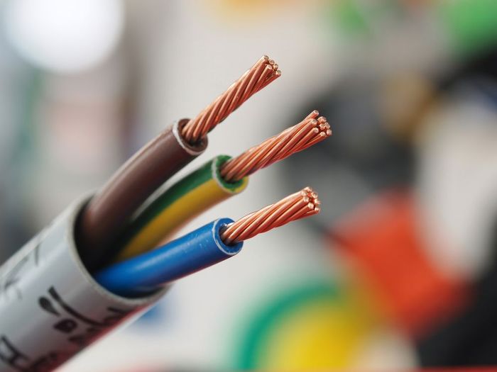 A close-up view of a multi-core electrical cable with brown, green-yellow, and blue insulated copper wires exposed.