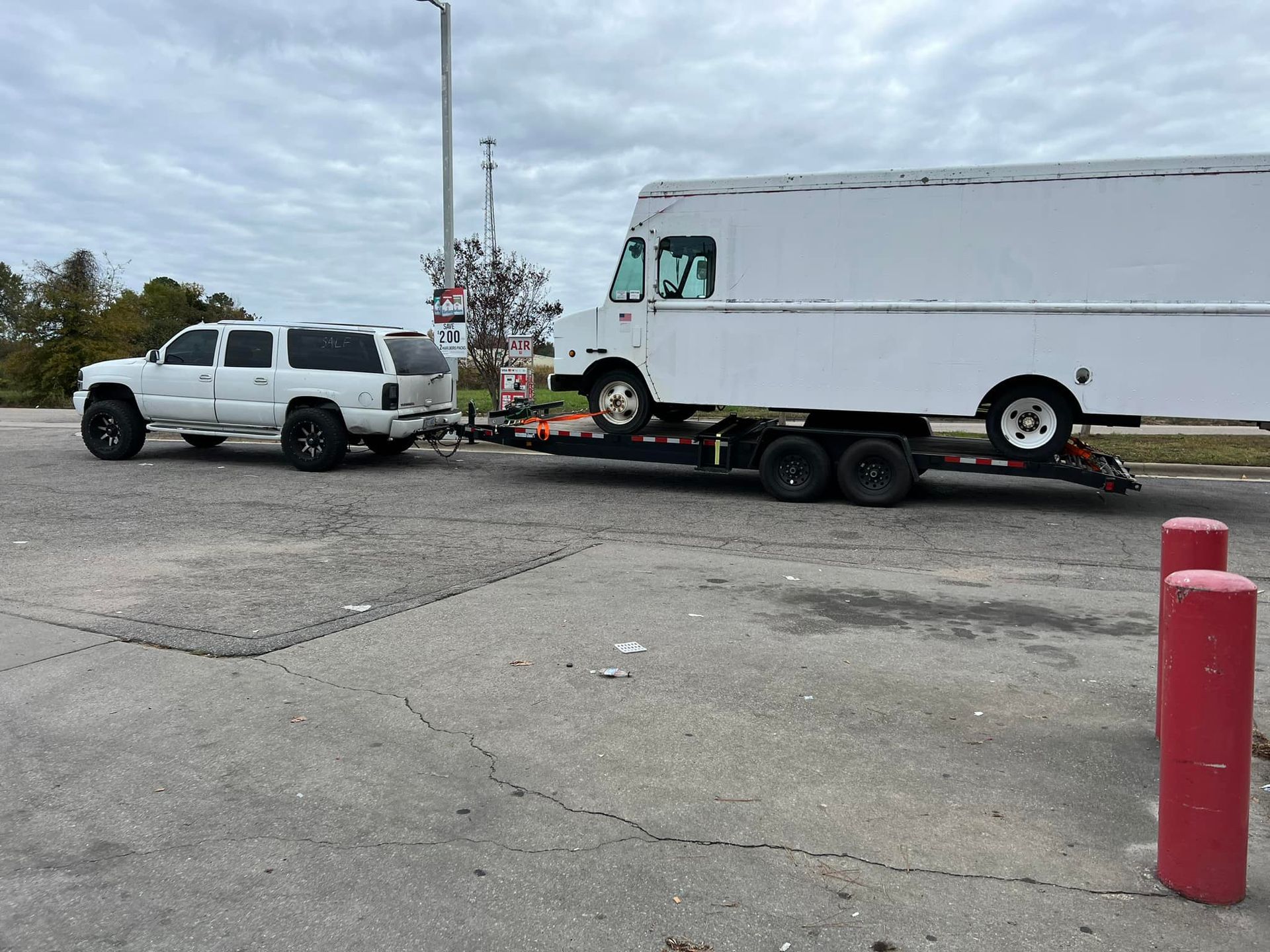 A white truck is towing a white van on a trailer.