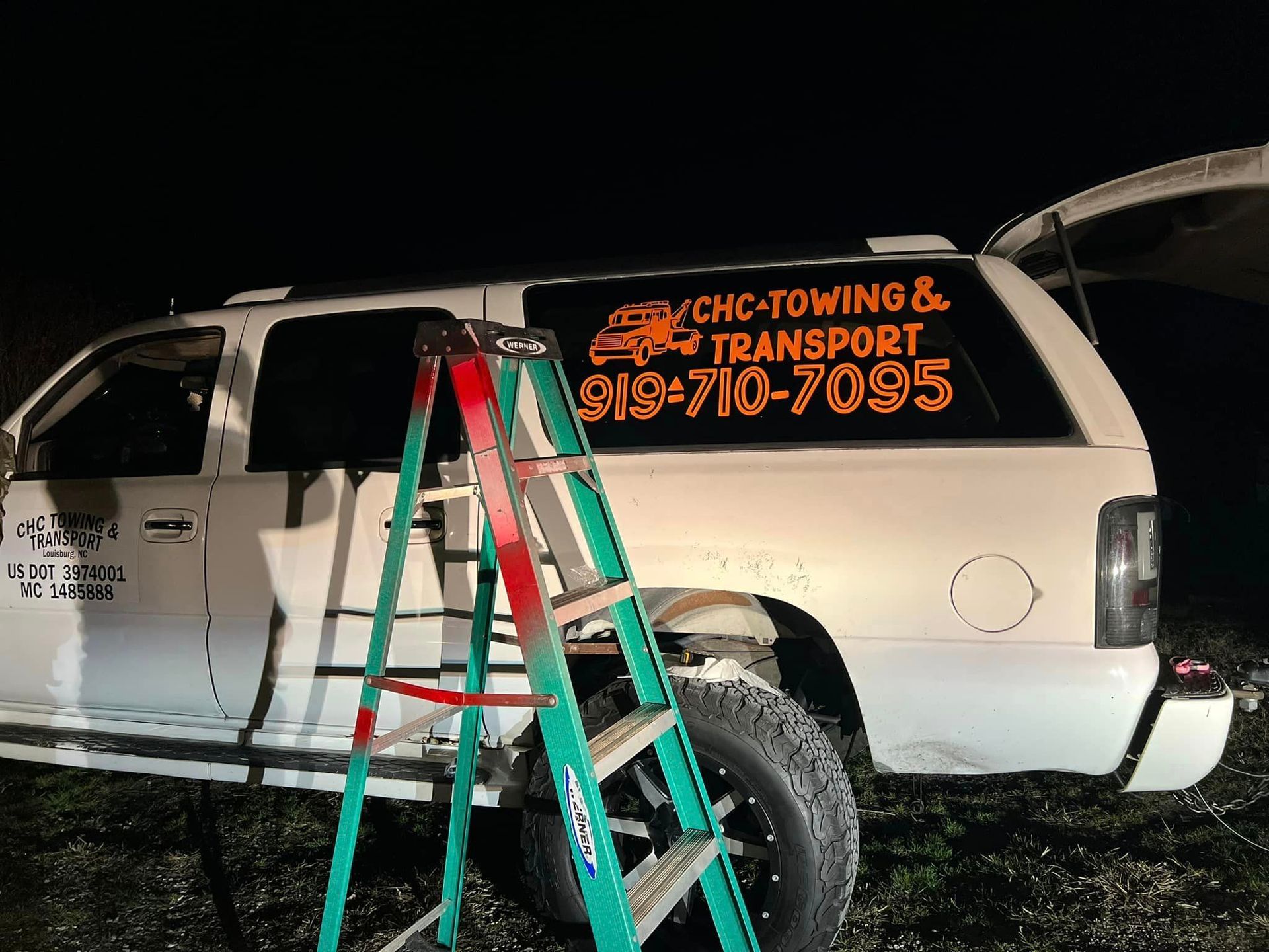 A ladder is sitting next to a white truck that says cnc towing and transport.