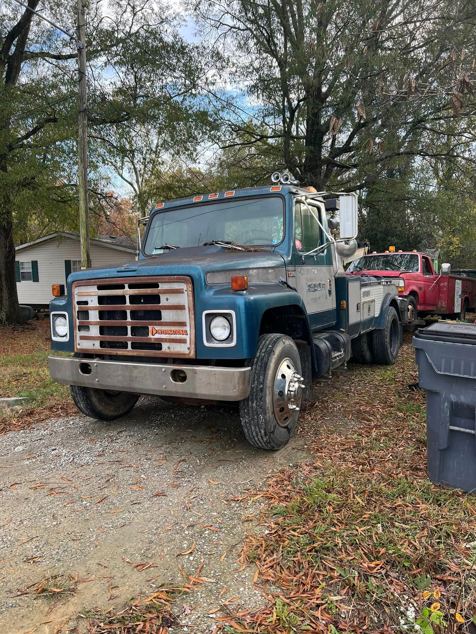 A blue tow truck is parked in a gravel lot next to a red truck.