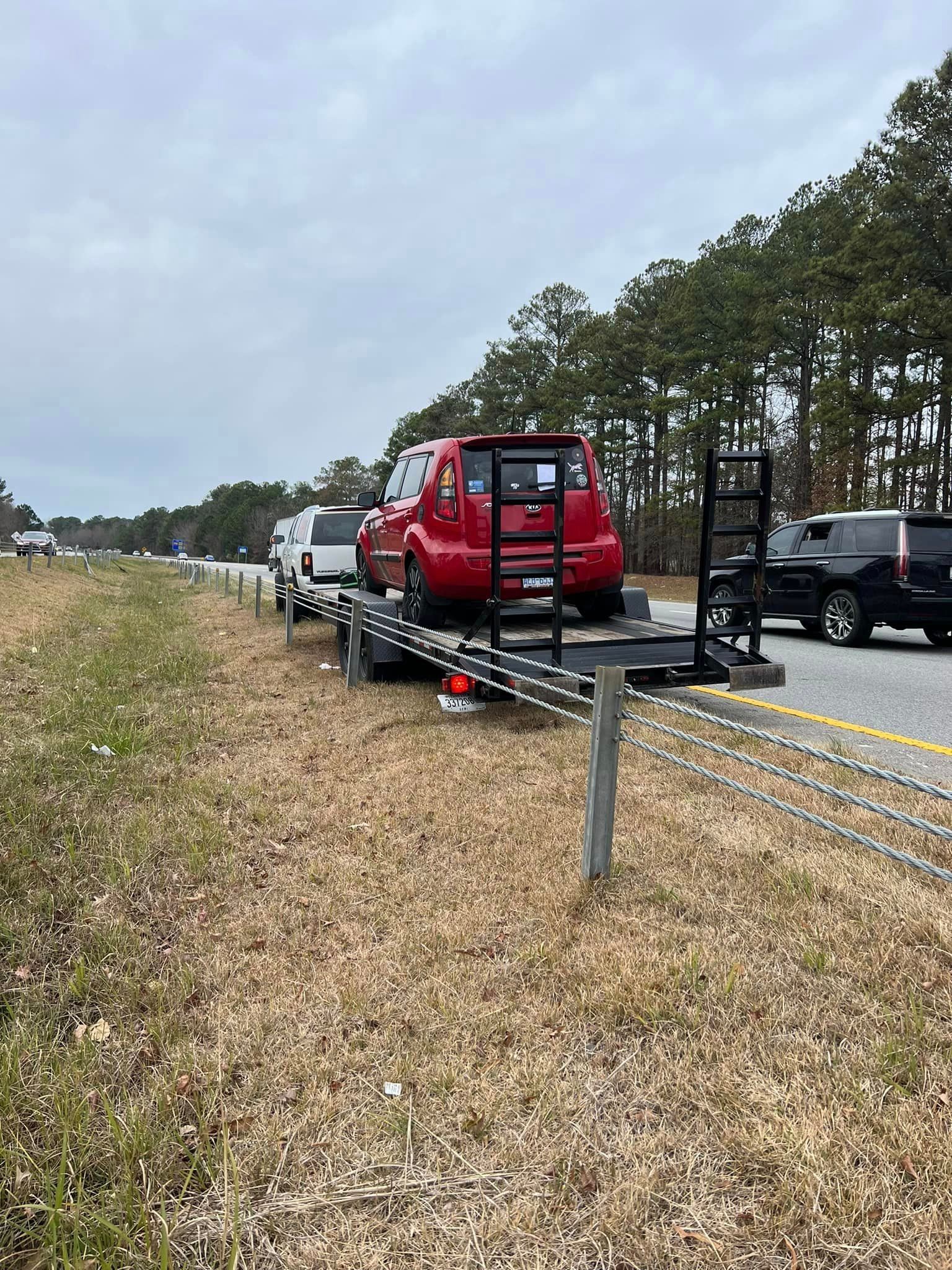 A red suv is being towed down a highway on a trailer.