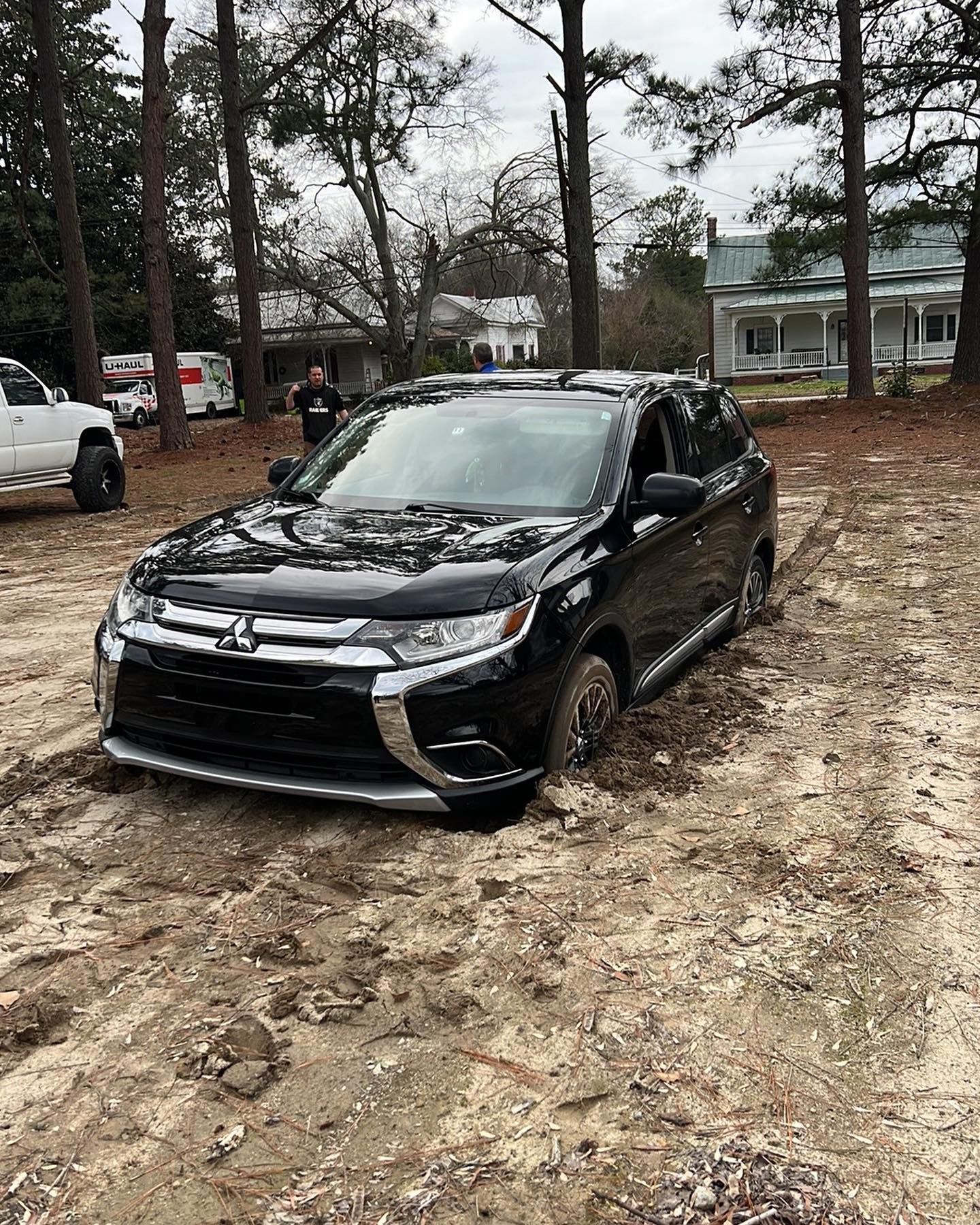 A black car is stuck in the mud in a muddy field.