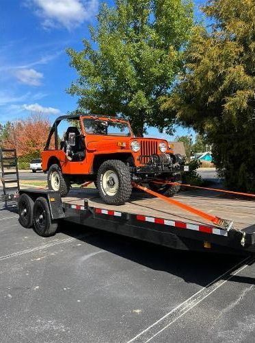 A jeep is being towed on a trailer in a parking lot.