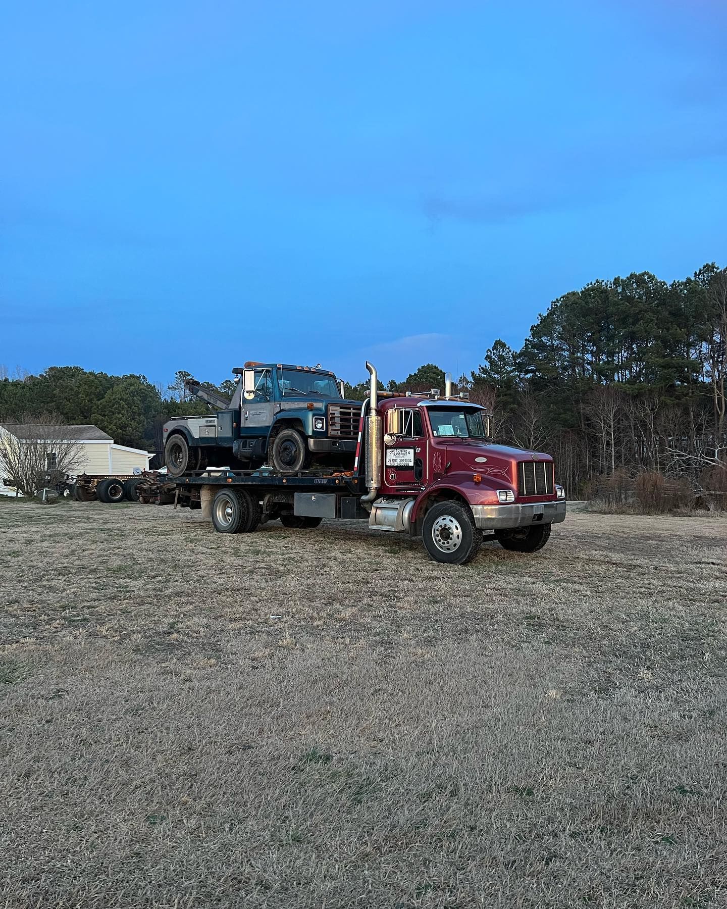 A tow truck is carrying a jeep and a truck in a field.