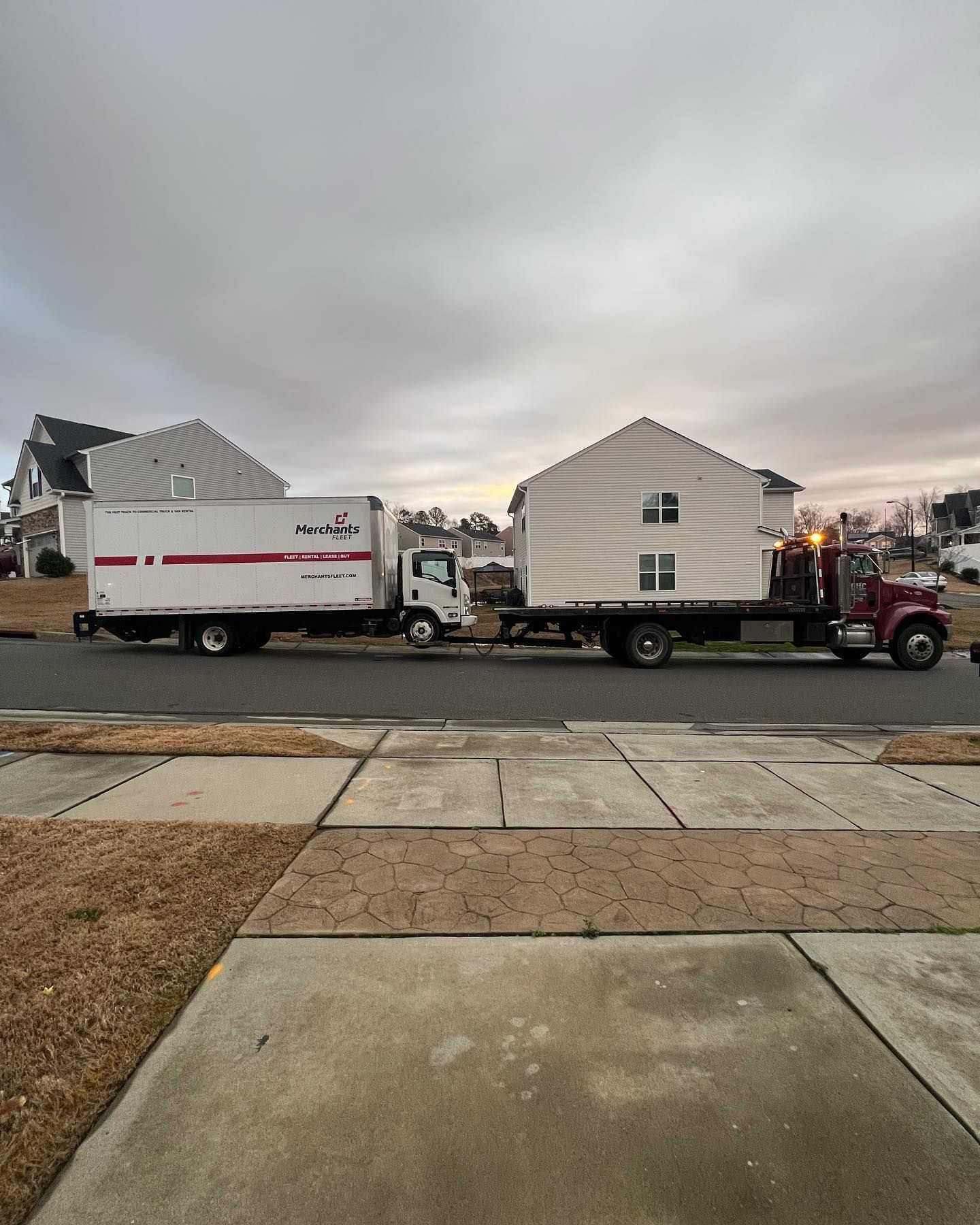A white truck is pulling a white house down a street.