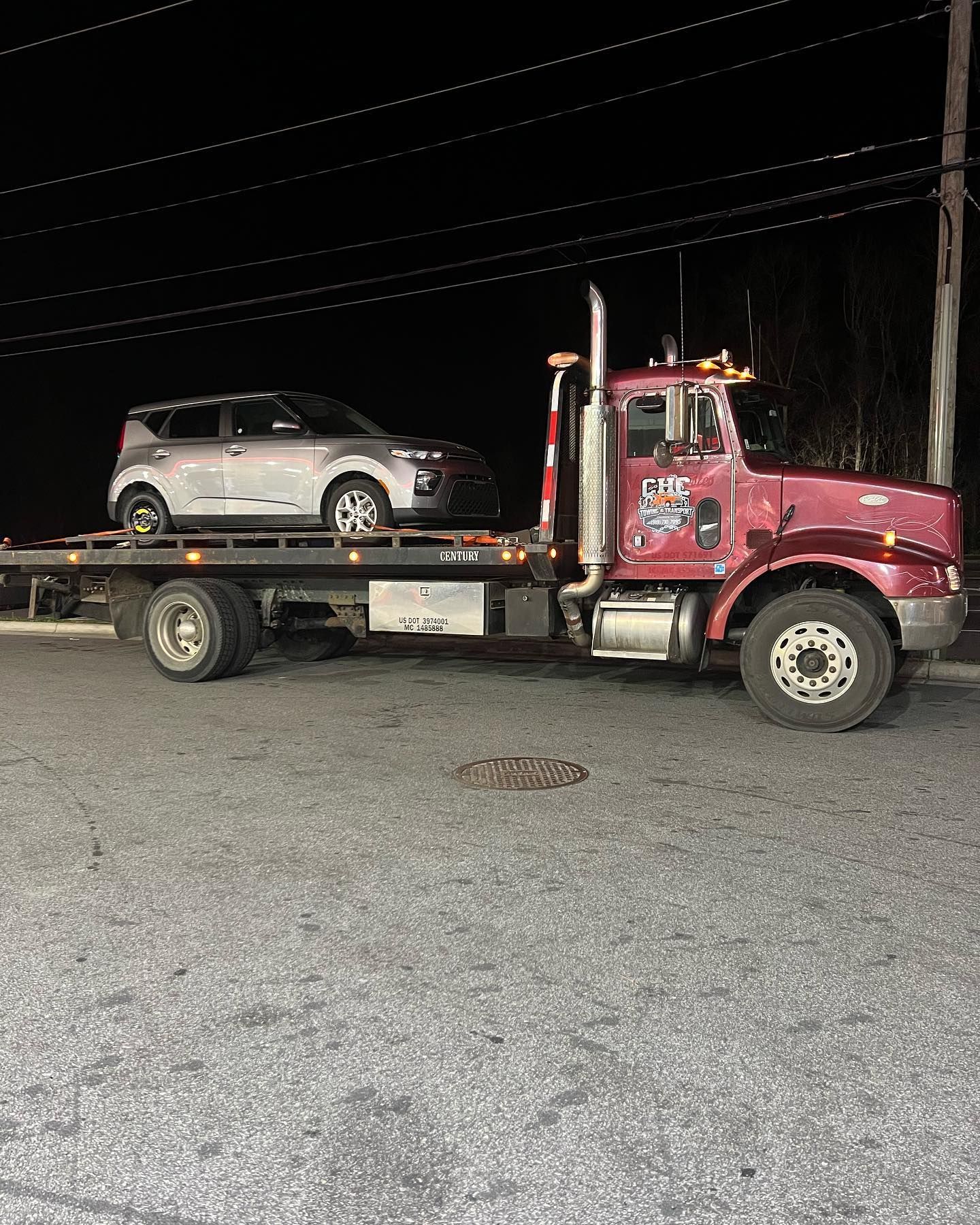 A red tow truck is towing a car in a parking lot at night.