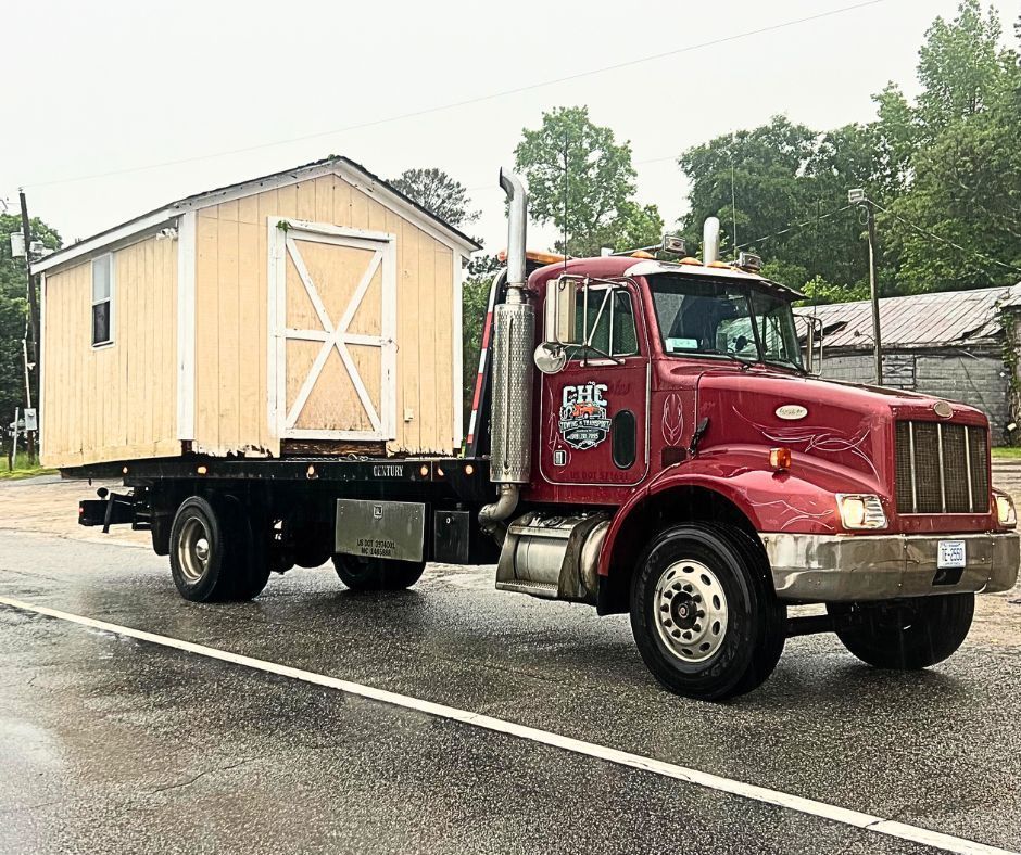 A red tow truck is carrying a small house on a trailer.