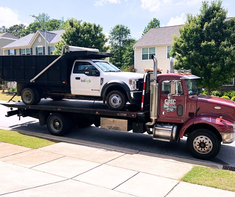 A red tow truck is carrying a dump truck and a white truck.