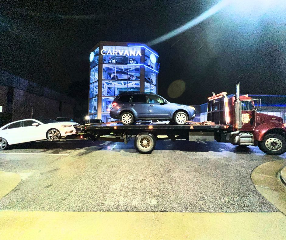 A tow truck is carrying cars to a car wash