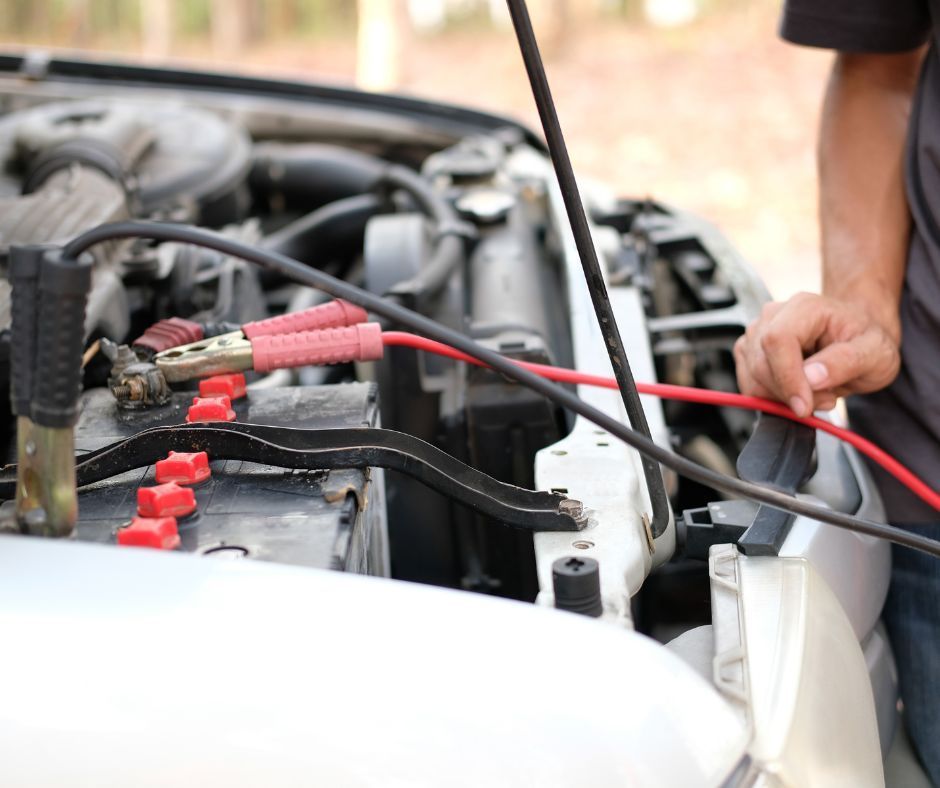 A man is charging a car battery with jumper cables