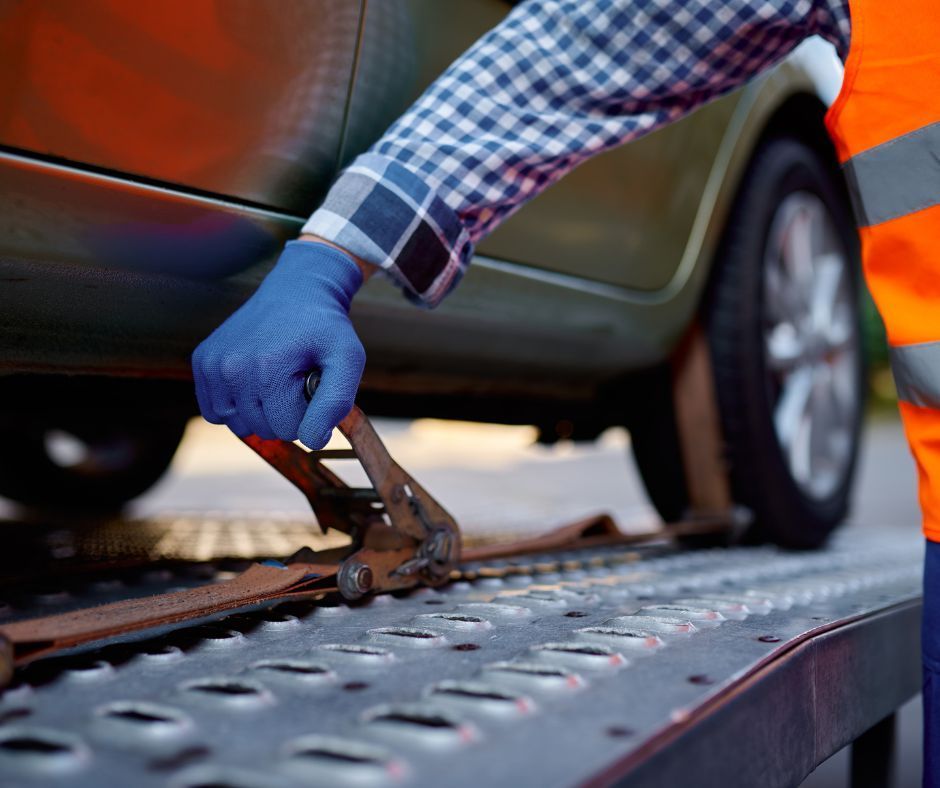 A man is using a pair of pliers to tie a car to a tow truck.