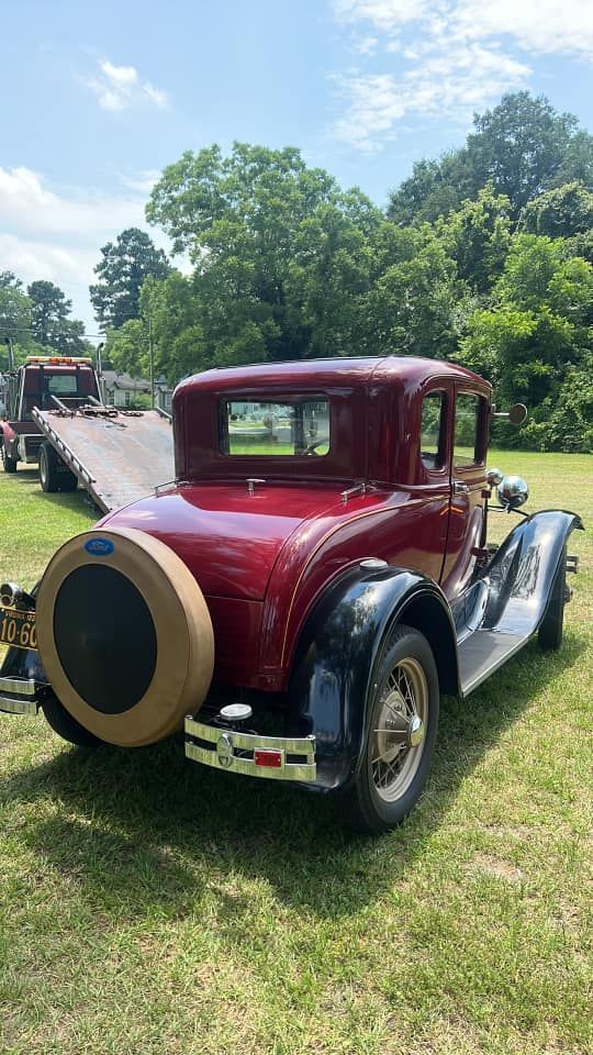 An old red car is parked in a grassy field next to a tow truck.