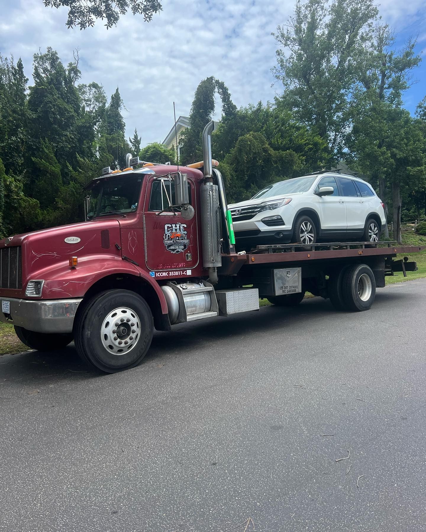 A red tow truck is carrying a white suv on the back of it.