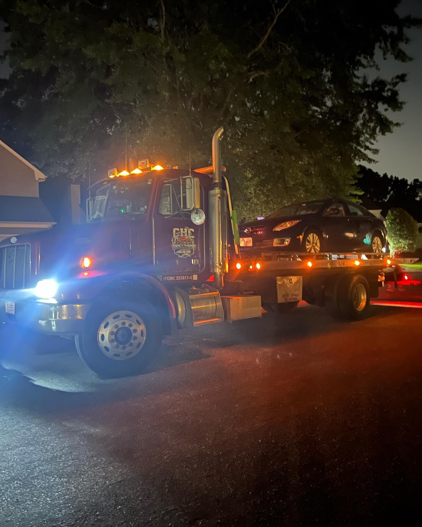 A tow truck is towing a black car at night.