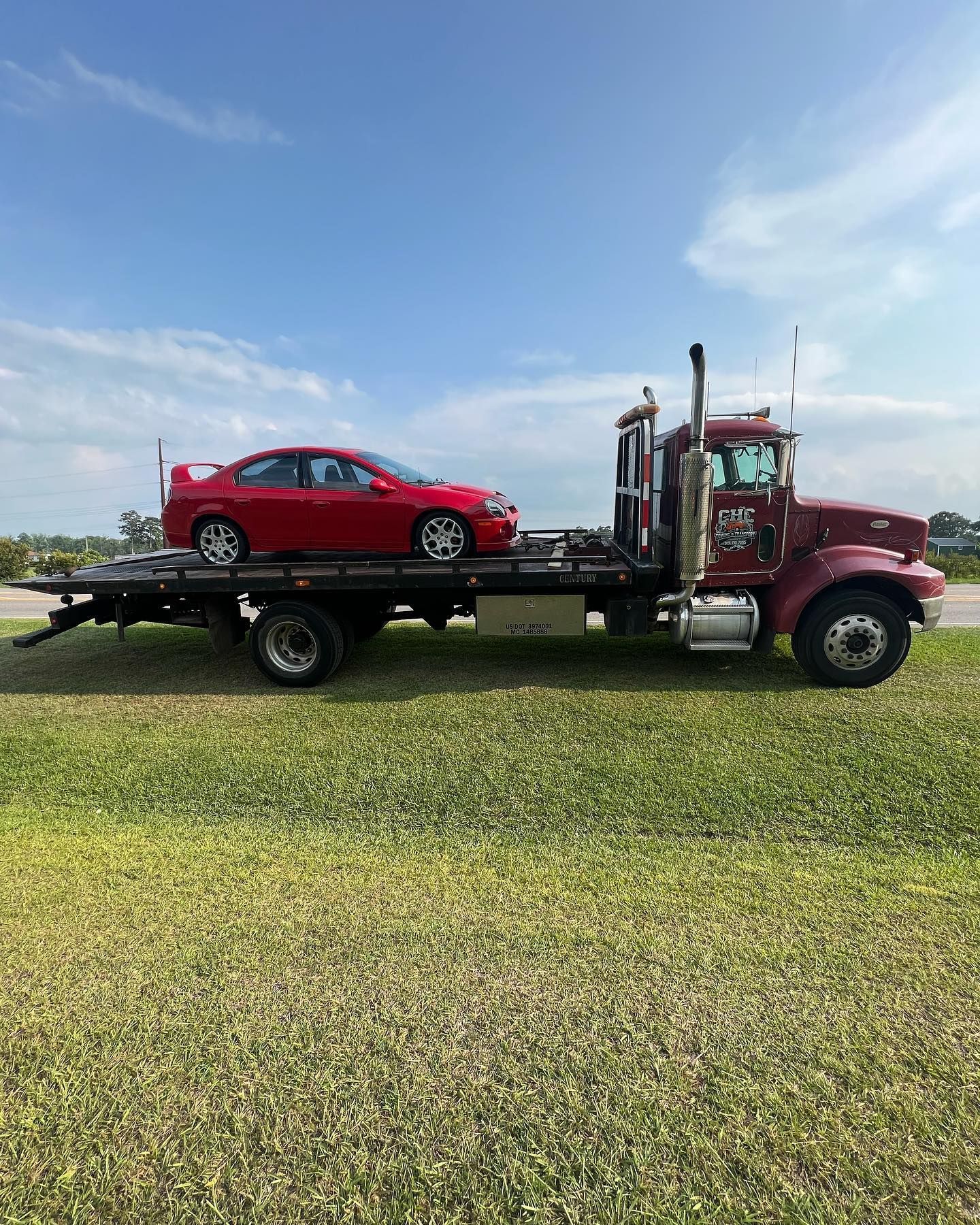 A red tow truck is towing a red car in a grassy field.