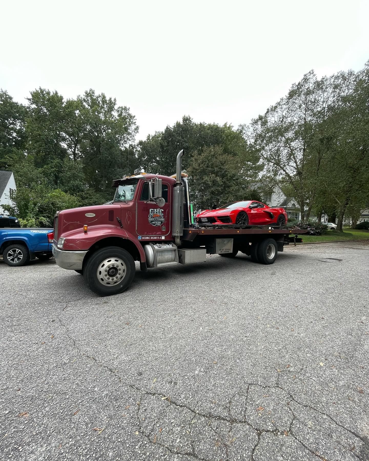 A red tow truck is towing a red sports car in a parking lot.