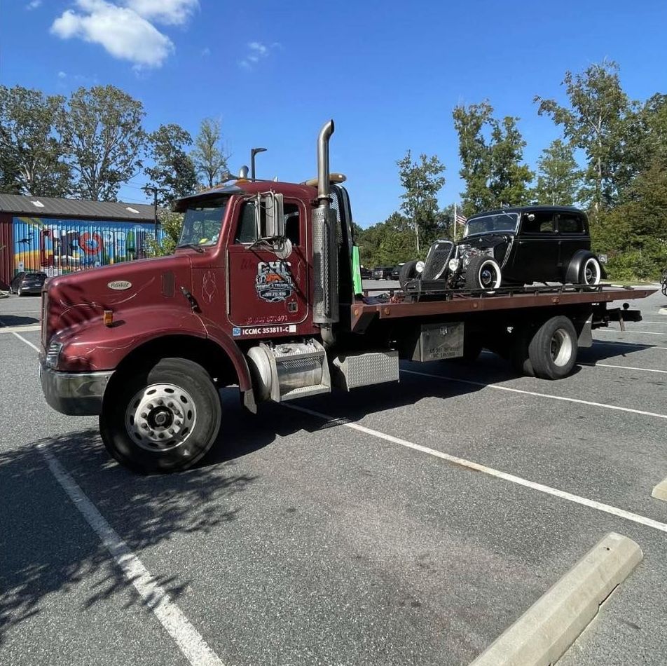 A red tow truck with a black car on the back is parked in a parking lot