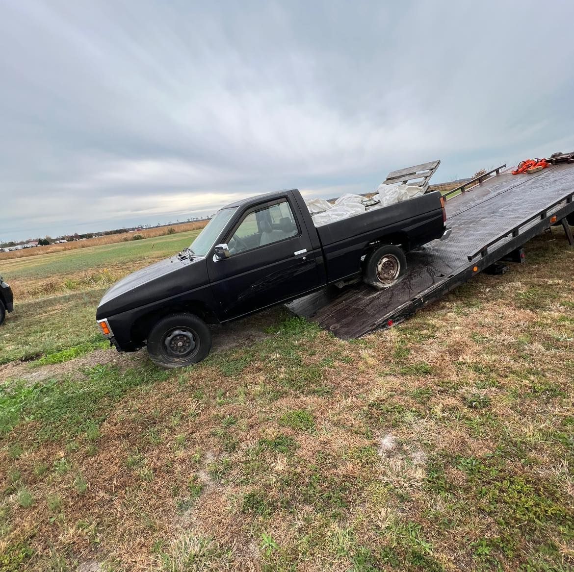 A black truck is sitting on top of a tow truck in a field.