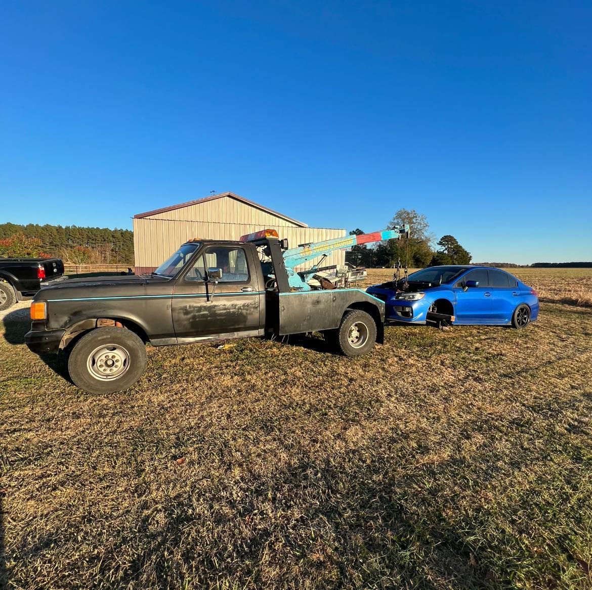 A tow truck is towing a blue car in a field.