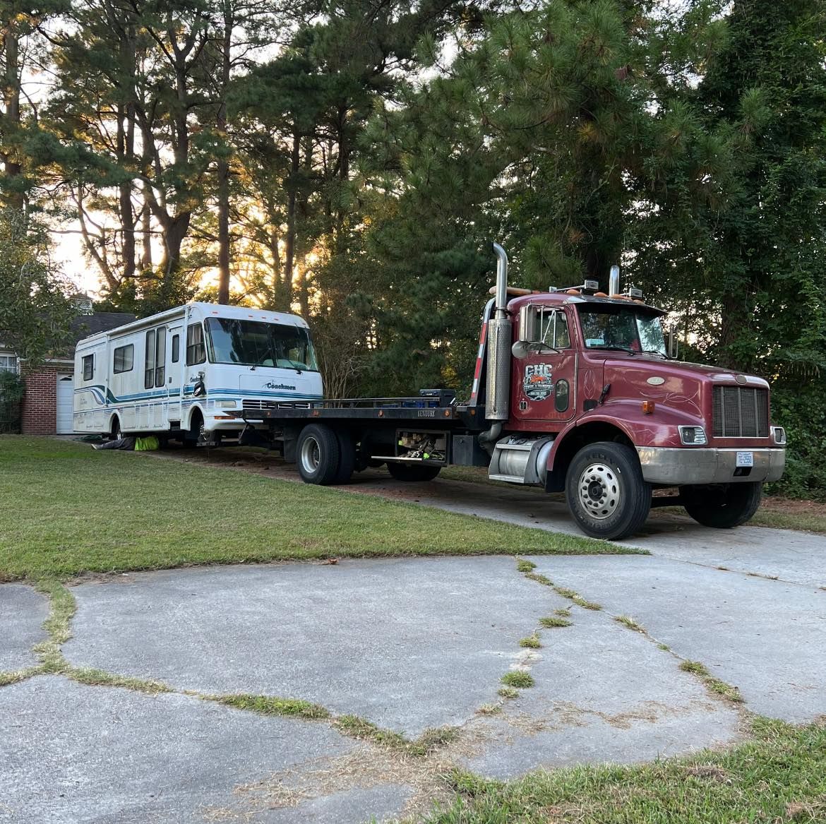 A red tow truck is towing a rv in a driveway.