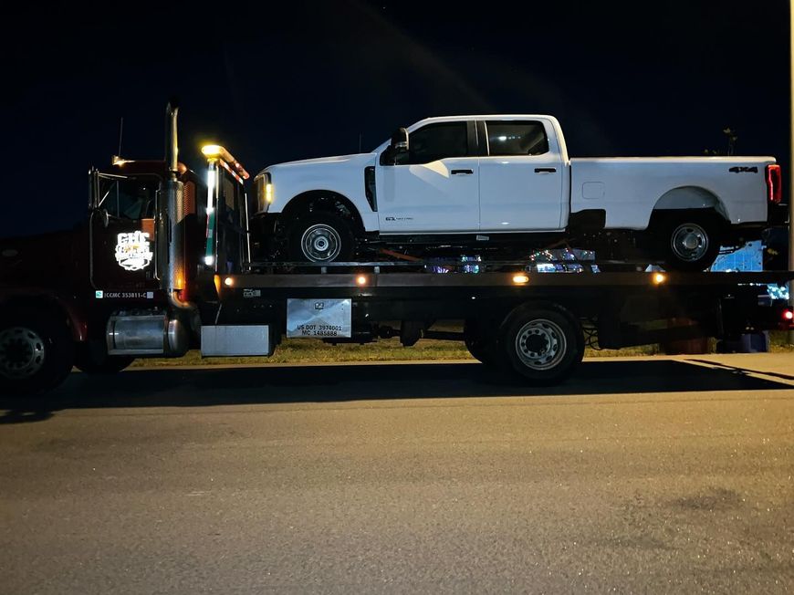 A white truck is being towed by a tow truck at night.