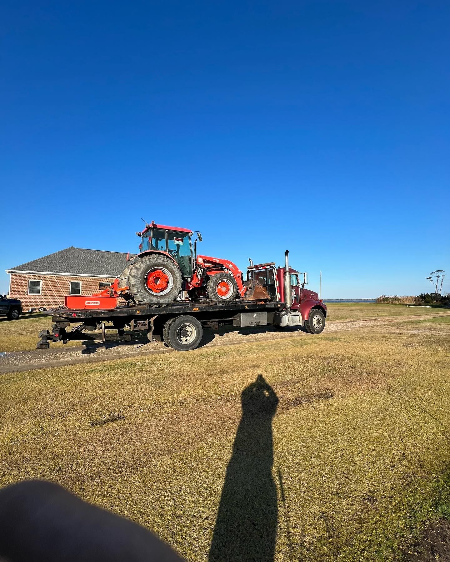 A tow truck is carrying two tractors in a field.
