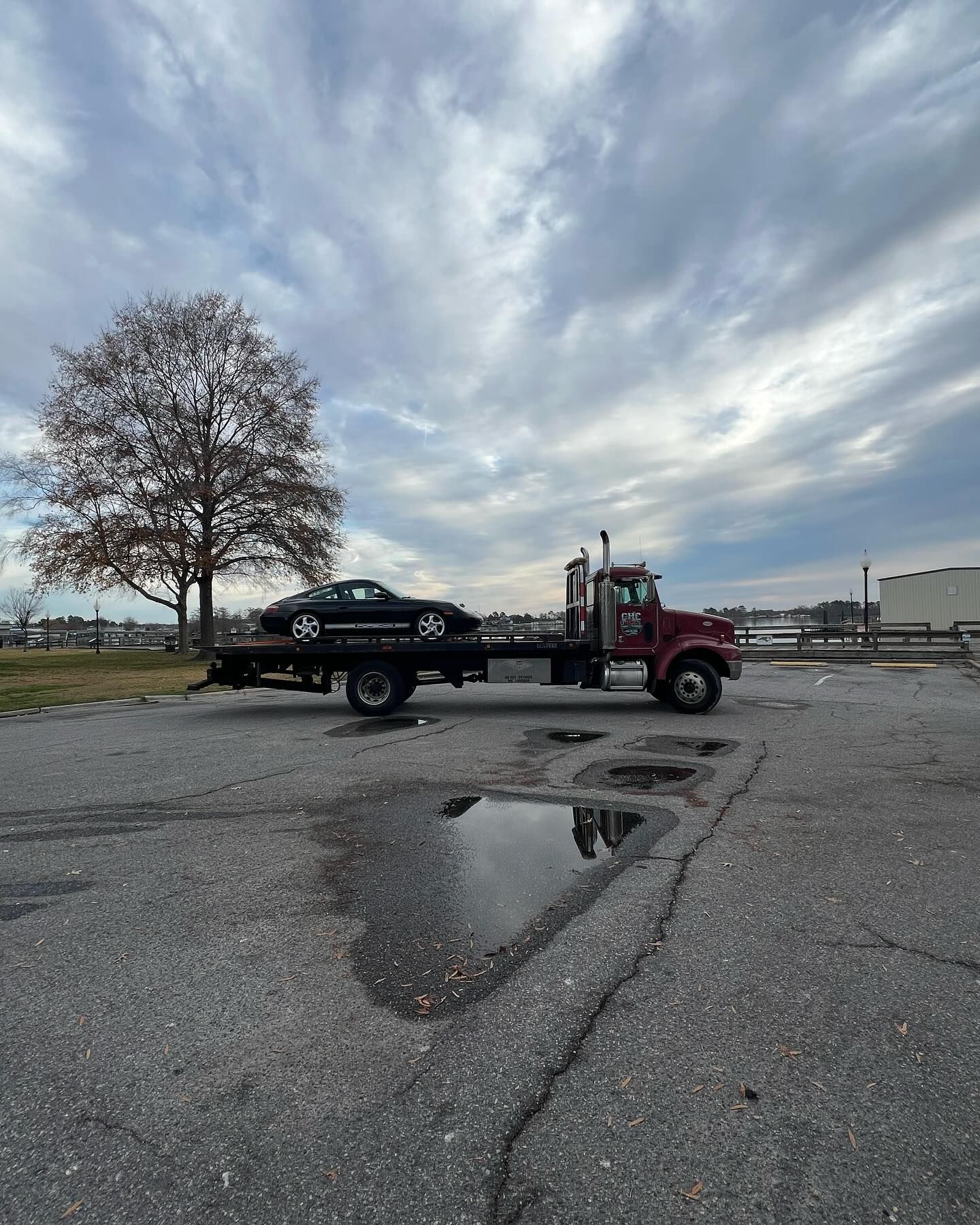 A red tow truck is towing a black car in a parking lot.