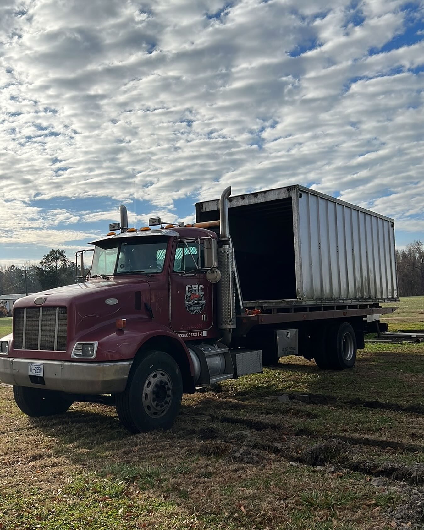A red semi truck with a white trailer is parked in a field.
