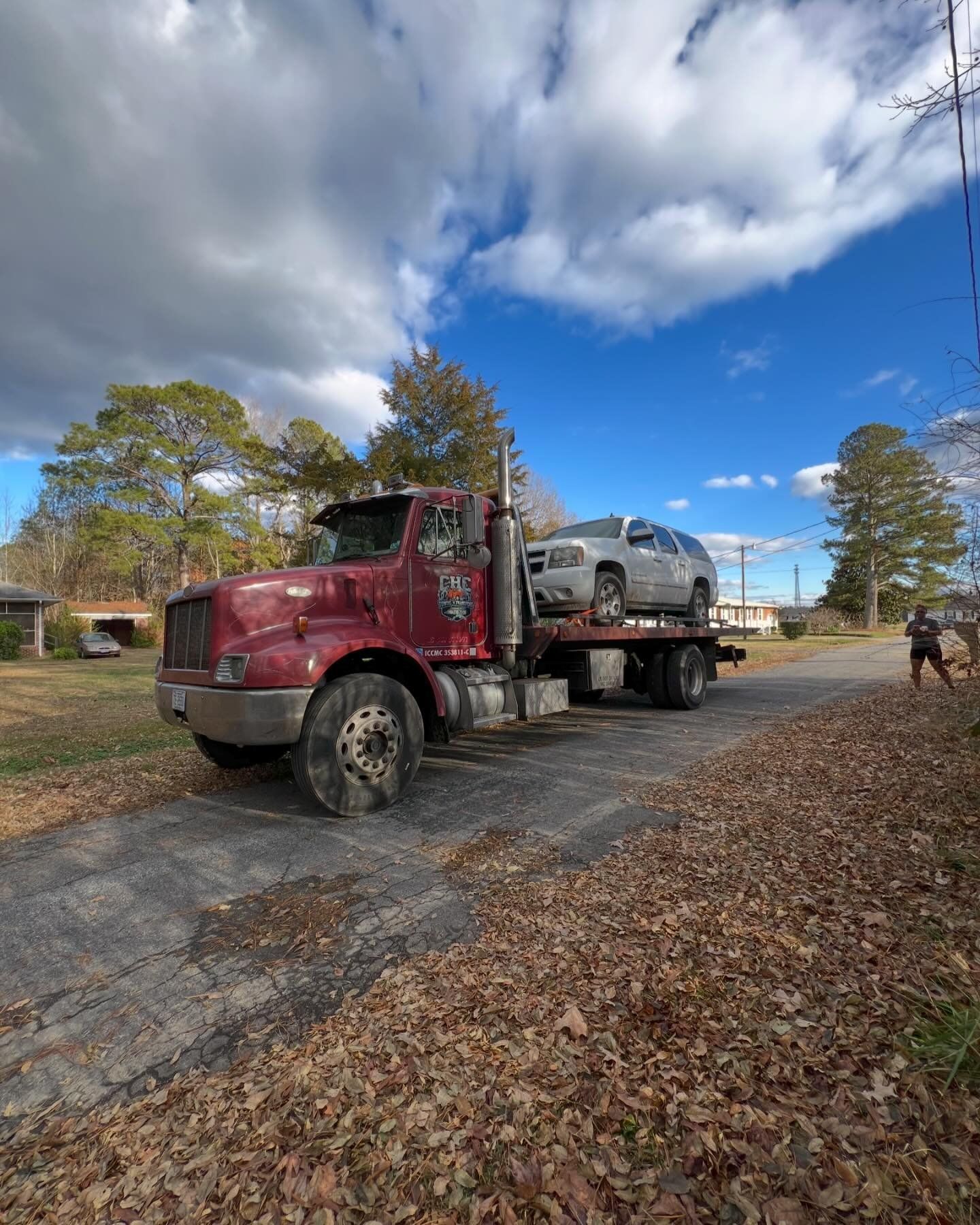 A red tow truck is carrying two cars down a road.